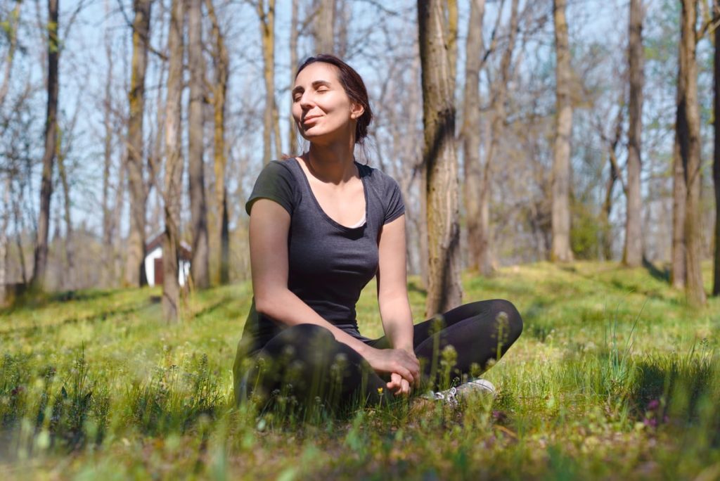 A woman sits outdoors and practicing mindfulness meditation.