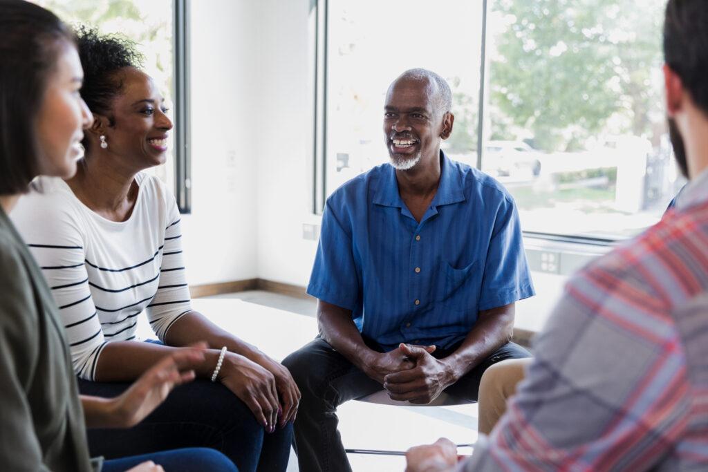 Mature African American man smile while discussing something with the people in his support group.