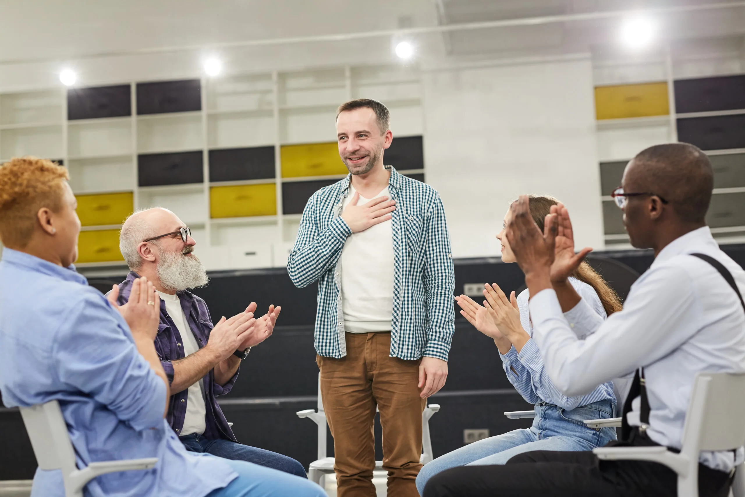 Portrait of smiling mature man    introducing himself during therapy session in support group to people clapping, copy space
