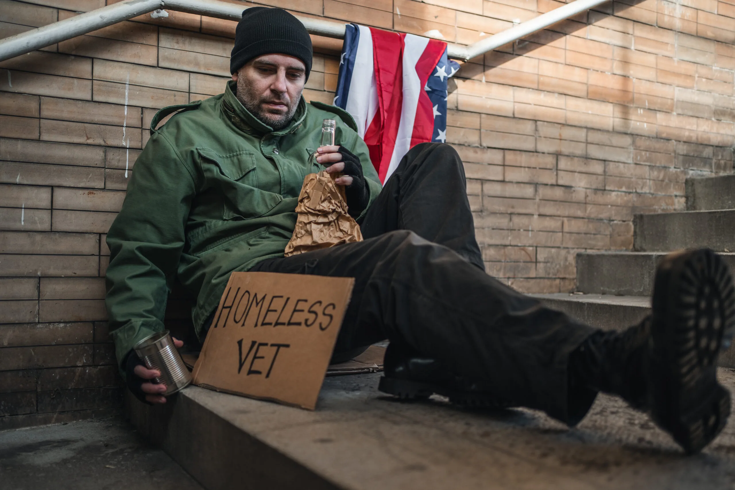 Homeless army veteran sitting on pavement begging on the street holding a placard with text Homeless vet